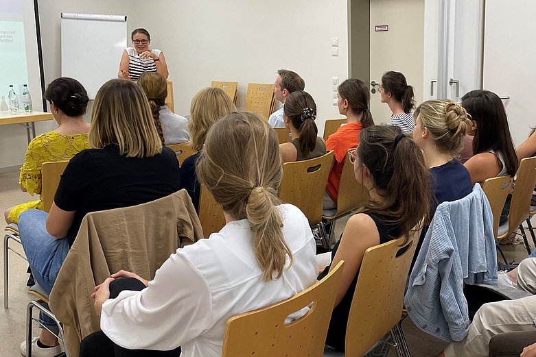 In einem Seminarraum hören viele Zuhörerinnen der Professorin zu.